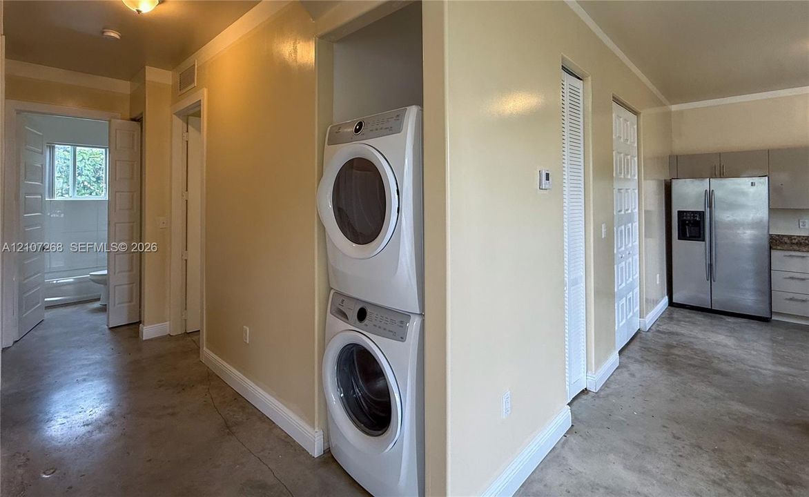 Built-in laundry closet with stacked washer and dryer, polished concrete flooring, louvered closet doors, and crown molding