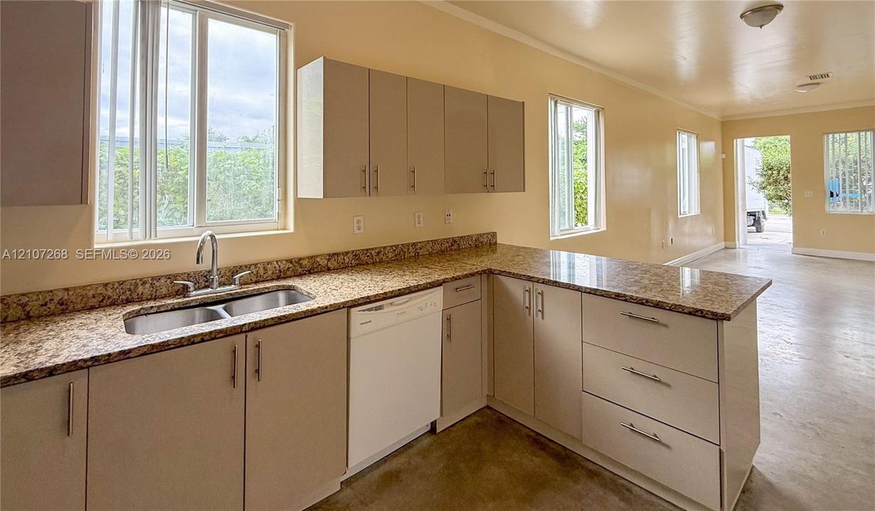 Kitchen featuring light-toned flat-panel cabinetry, stone-finish countertops, stainless steel dual-basin undermount sink with arched faucet, built-in dishwasher, and multiple windows
