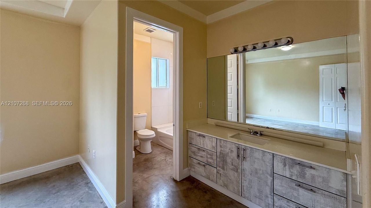 Bathroom featuring a custom vanity with a solid-surface integrated countertop, full-width wall mirror, multi-bulb overhead lighting, and polished concrete flooring