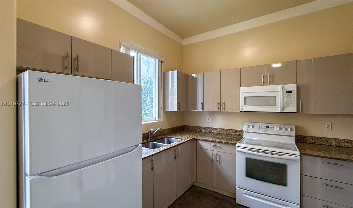 Kitchen featuring high-gloss cabinetry, stone-finish countertops, dual-basin stainless steel sink, and built-in microwave