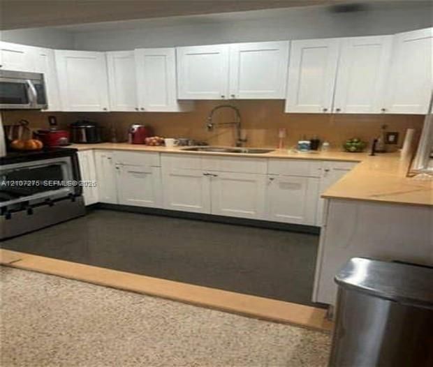 Kitchen featuring white shaker-style cabinetry, solid-surface countertops, stainless steel undermount sink, gooseneck faucet, and stainless steel range