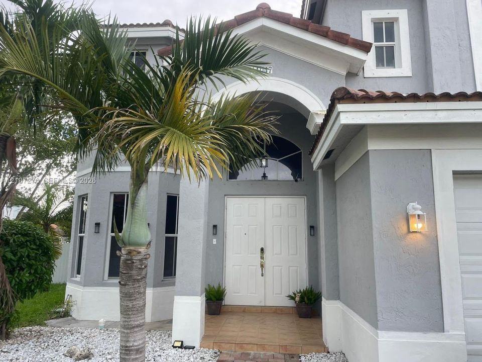 Stucco exterior featuring an arched entryway, double-door entrance, tile flooring, arched transom window, and tiled roof