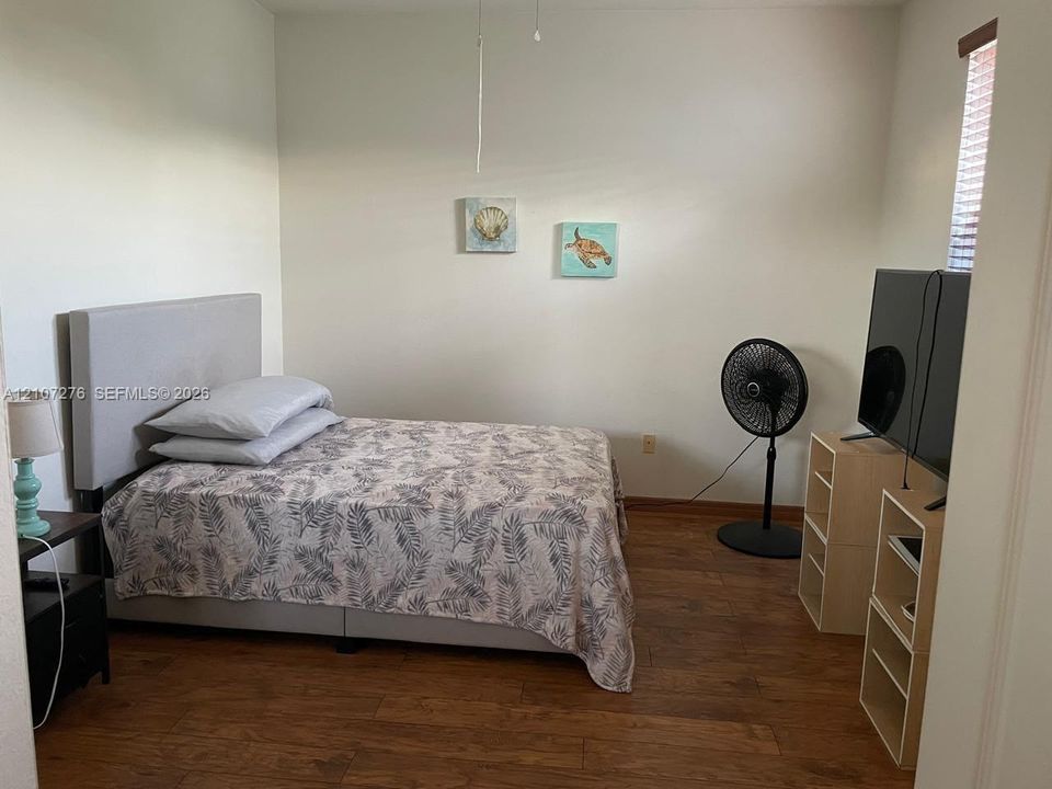 Room featuring wood-finish flooring, neutral wall paint, and a ceiling-mounted light fixture with a pull cord