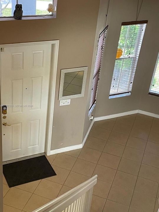 Entry area featuring tiled flooring, high ceilings, multiple tall windows with horizontal blinds, and a transom window