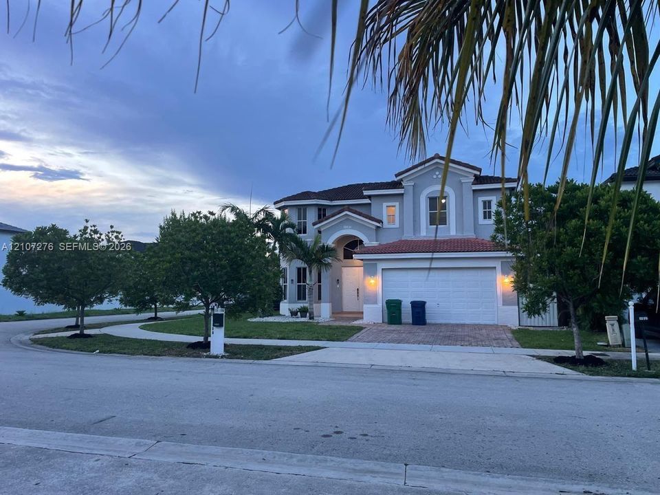 Two-story stucco exterior featuring a tiled roof, multi-gabled facade, arched entryway, and an attached two-car garage with a paved driveway
