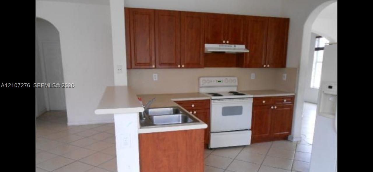 Kitchen featuring wood cabinetry, a breakfast bar, a stainless steel double-basin sink, and tile flooring