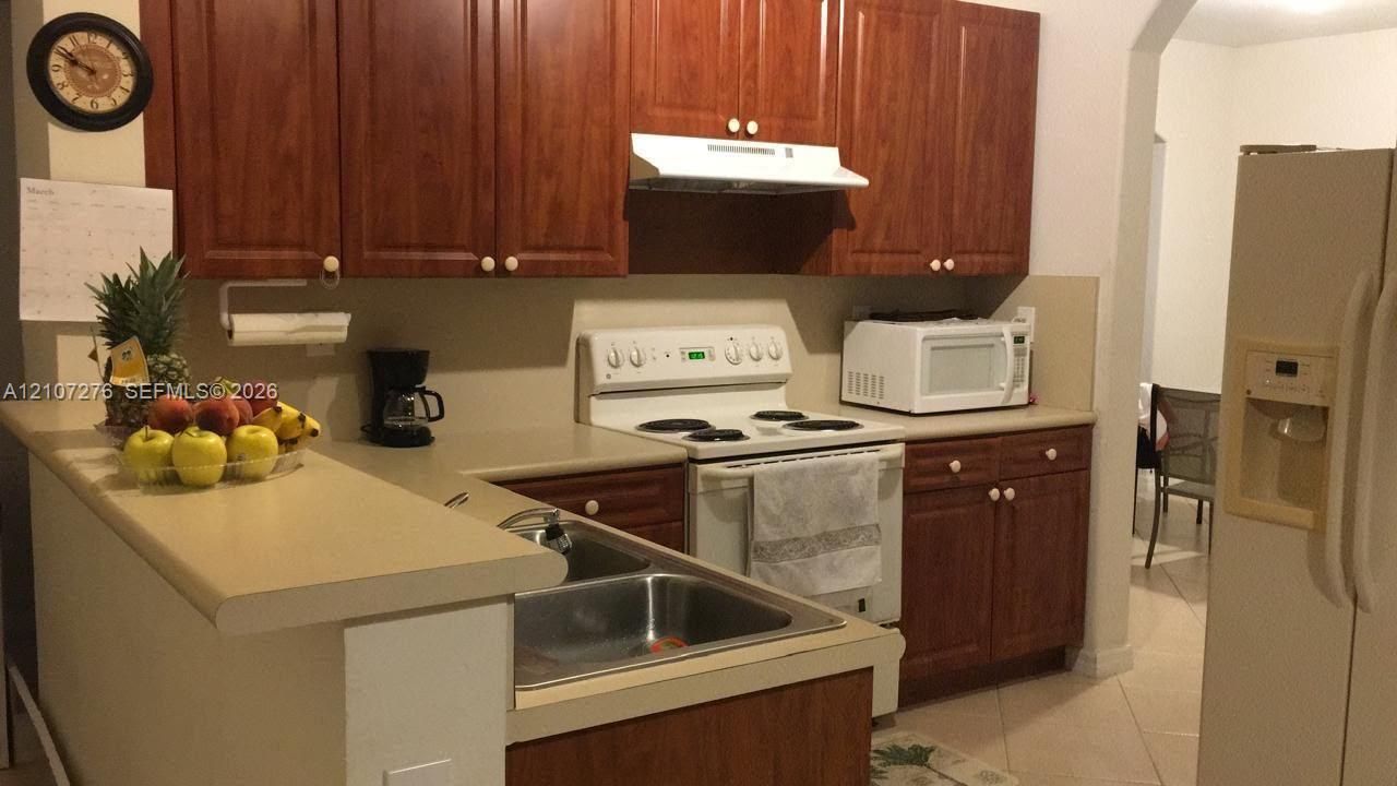 Kitchen featuring raised-panel wood cabinetry, solid-surface countertops, dual-basin stainless steel sink, and tile flooring