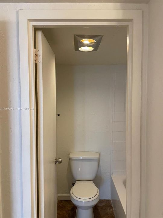 White porcelain commode and recessed ceiling lighting featuring a square-frame fixture