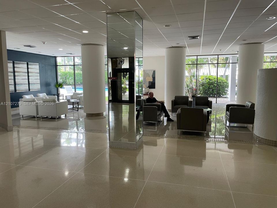 Common area featuring polished stone-finish flooring, floor-to-ceiling windows, structural columns, and a central mirrored pillar