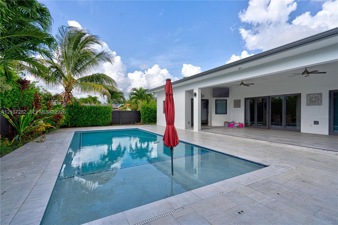 Outdoor patio featuring a covered lanai with ceiling fans, an integrated rectangular swimming pool, and stone-finish paving