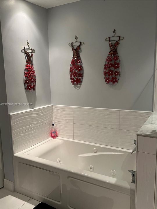Jetted soaking tub featuring a white surround and textured horizontal tile backsplash
