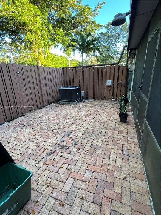 Private patio featuring herringbone-patterned brick pavers and a tall wood-slat privacy fence