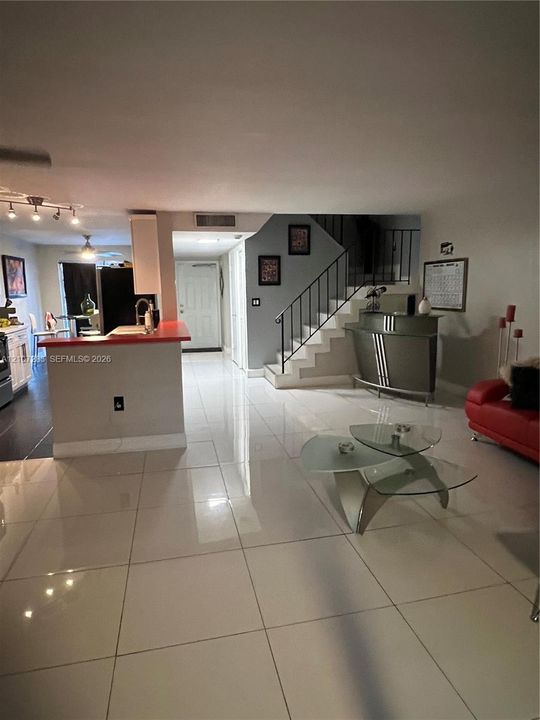 Large-format porcelain tile flooring, breakfast bar with a solid surface countertop, and a staircase featuring metal railings