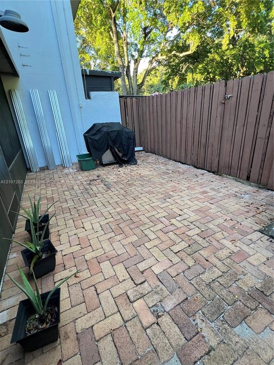 Private outdoor patio featuring herringbone-patterned brick pavers and a perimeter wood privacy fence