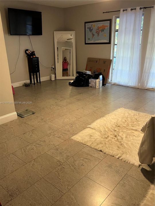 Living area featuring neutral-toned tile flooring and glass paneled doors with a curtain rod fixture