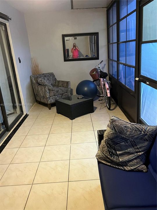 Enclosed porch featuring large-format ceramic floor tiles, multi-pane floor-to-ceiling windows with black framing, and sliding glass entry door