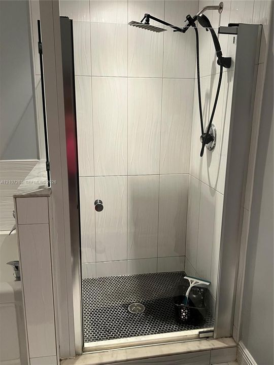 Walk-in shower featuring a frameless glass door, textured white wall tile, dark penny-round floor tile, and a dual-head rainfall shower fixture