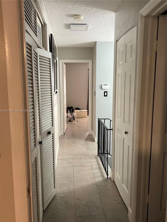Hallway featuring large-format tile flooring, white bi-fold closet doors, louvered closet cabinetry, and a black metal railing