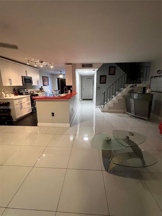 Kitchen featuring white cabinetry, solid-surface countertops, and built-in stainless steel appliances, complemented by large-format tile flooring and an open staircase with wrought-iron railing