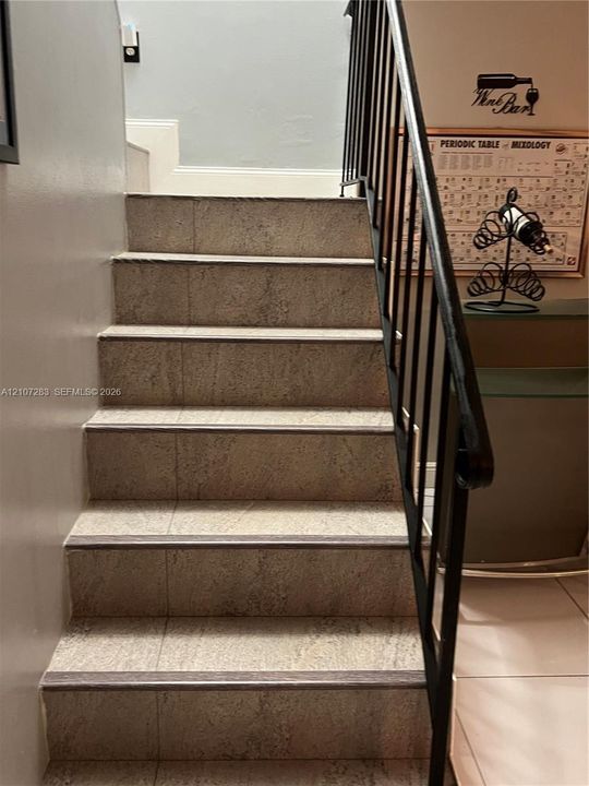 Staircase featuring stone-textured treads, dark metal railings, and neutral wall tones