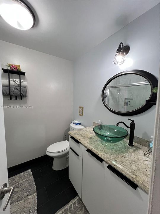 Stone countertop with a glass vessel sink, matte black faucet, oval wall mirror, and dark tile flooring