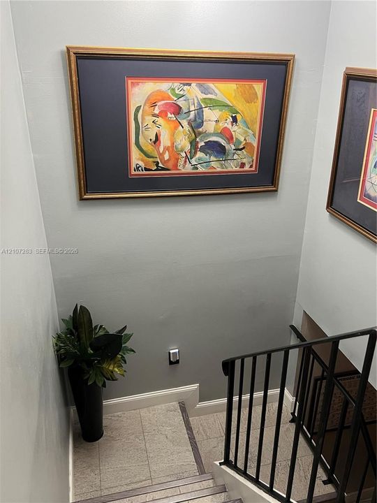 Staircase featuring neutral-toned wall paint, stone-finish treads, and a matte black metal railing