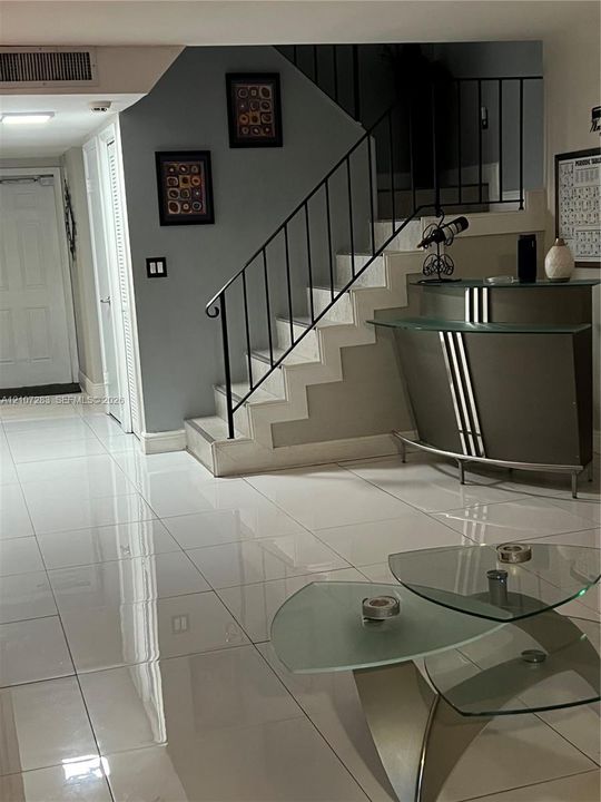 Large-format polished tile flooring, staircase with a black metal railing, and crisp neutral wall finish