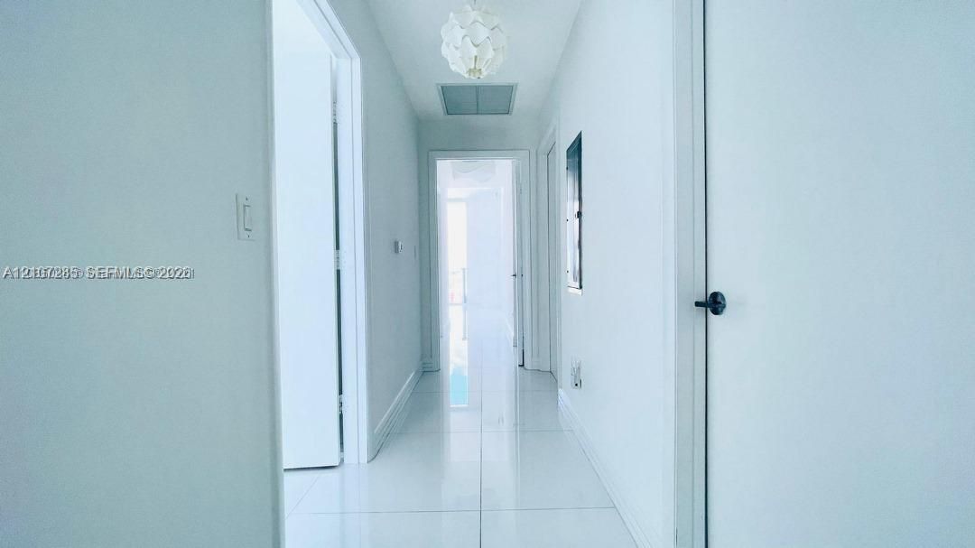 Hallway featuring high-gloss tile flooring, white interior doors with matte black hardware, and a contemporary spherical pendant light fixture