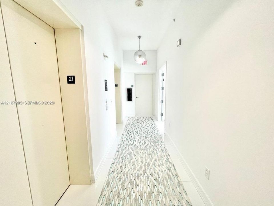 Hallway featuring neutral-toned walls, polished tile flooring, patterned runner carpet, and a spherical pendant light fixture