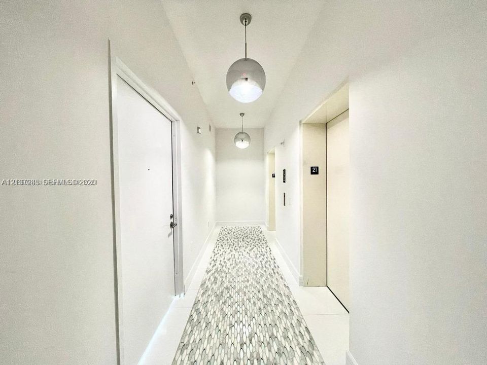 Hallway featuring crisp white walls, large-format tile flooring with a patterned mosaic inlay, and dual spherical pendant lighting fixtures