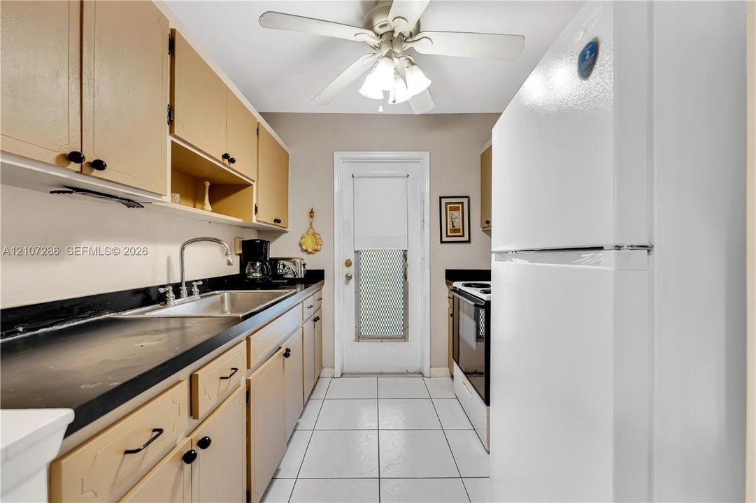 Kitchen featuring cabinetry with contrasting dark countertops, integrated stainless steel sink with goose-neck faucet, white tile flooring, and a ceiling-mounted light fixture with fan