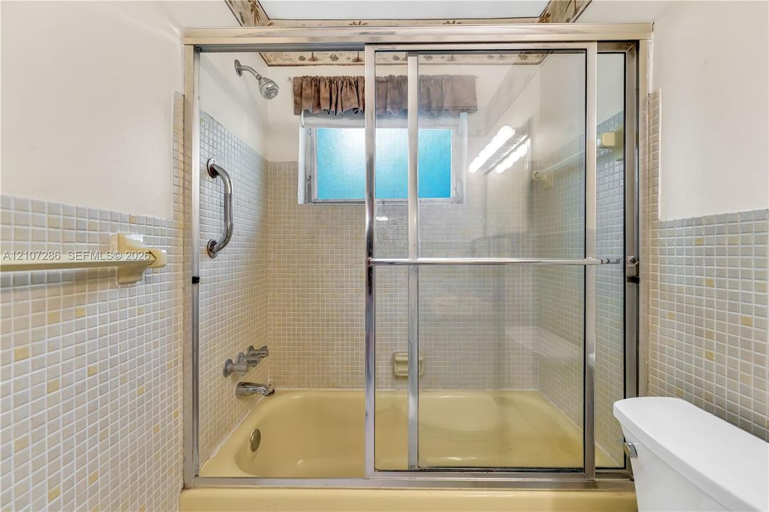 Bathtub featuring a glass sliding enclosure, mounted chrome faucet fixtures, and square mosaic wall tile surrounds