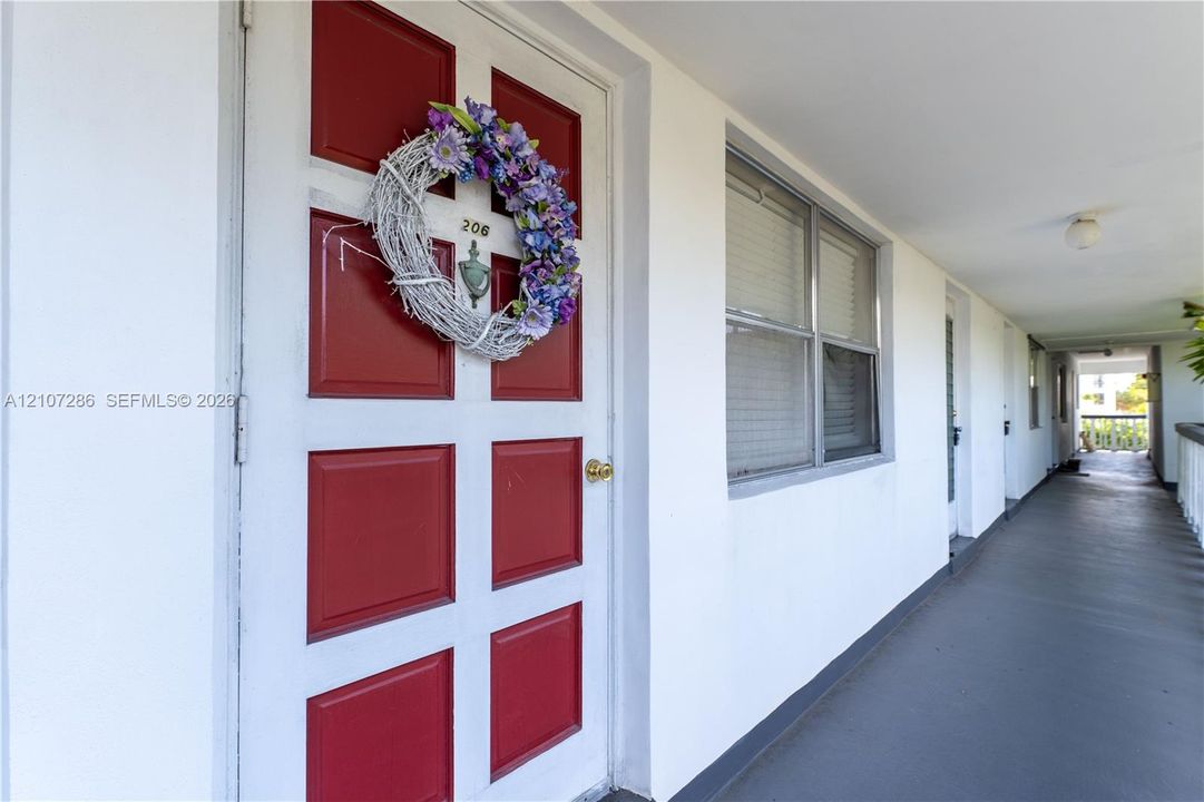 Red-painted six-panel entry door with metallic door knocker and brass-finish hardware, white stucco exterior wall, and window with white frame