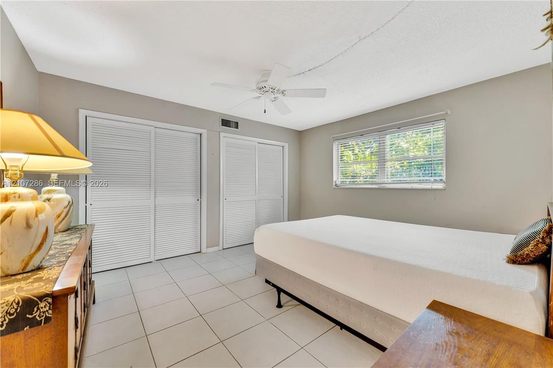 Ceramic tile flooring, dual louvered-style sliding closets, and a ceiling-mounted fan