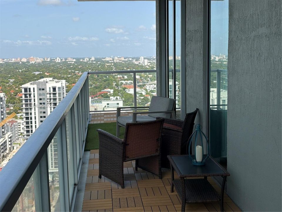 Covered private balcony with modular decking, glass panel railing, and expansive urban scenery