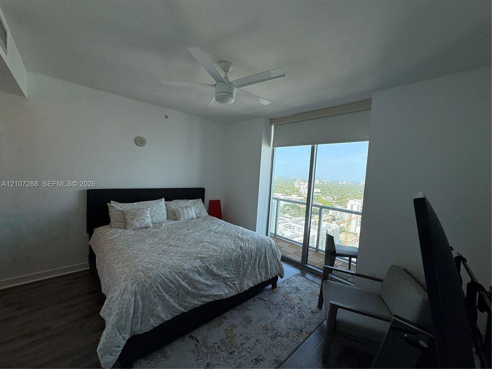Floor-to-ceiling glass sliding door, expansive balcony, wood-finish flooring, and white ceiling fan