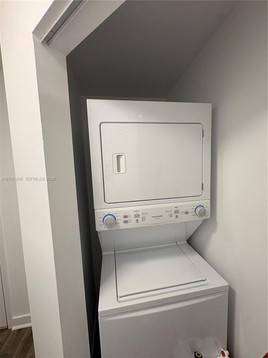 Stackable white laundry unit featuring a top-load washer and front-load dryer in a dedicated recessed closet