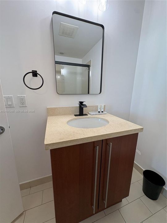 Vanity featuring a wood-finish cabinet with elongated hardware, a neutral-toned countertop with an integrated basin, a matte black faucet, and a rectangular mirror with a matching black frame