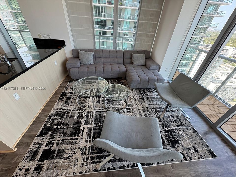 Floor-to-ceiling windows, wood-finish flooring, and kitchen island with black countertop