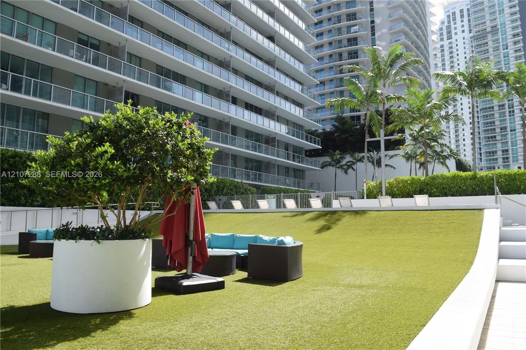 Elevated terrace featuring synthetic turf, concrete retaining walls, cylindrical planters, and glass-paneled balcony railings