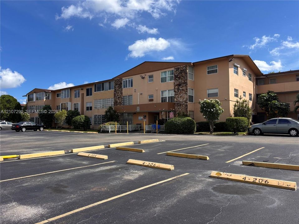Multi-story building exterior featuring smooth stucco finish, stone veneer accents, pitched rooflines, and ample dedicated surface parking