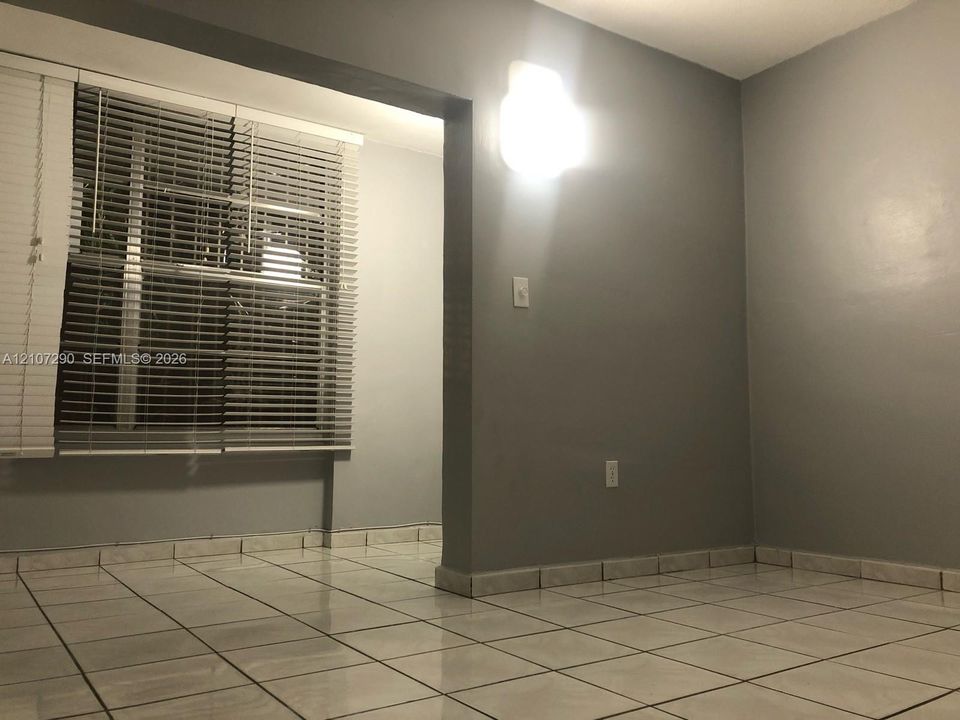 Neutral-toned interior featuring ceramic tile flooring, horizontal window blinds, and wall-mounted light fixture