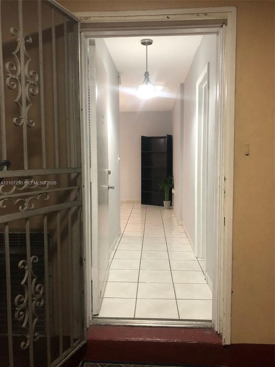 Entrance featuring a decorative metal security screen door, ceramic tile flooring, and a pendant light fixture