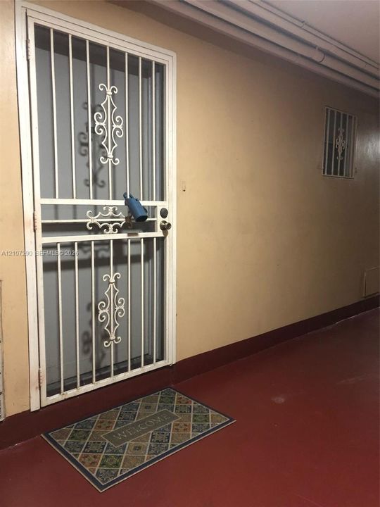 White metal security door featuring ornamental scrollwork details and a secondary window opening with matching metal security bars