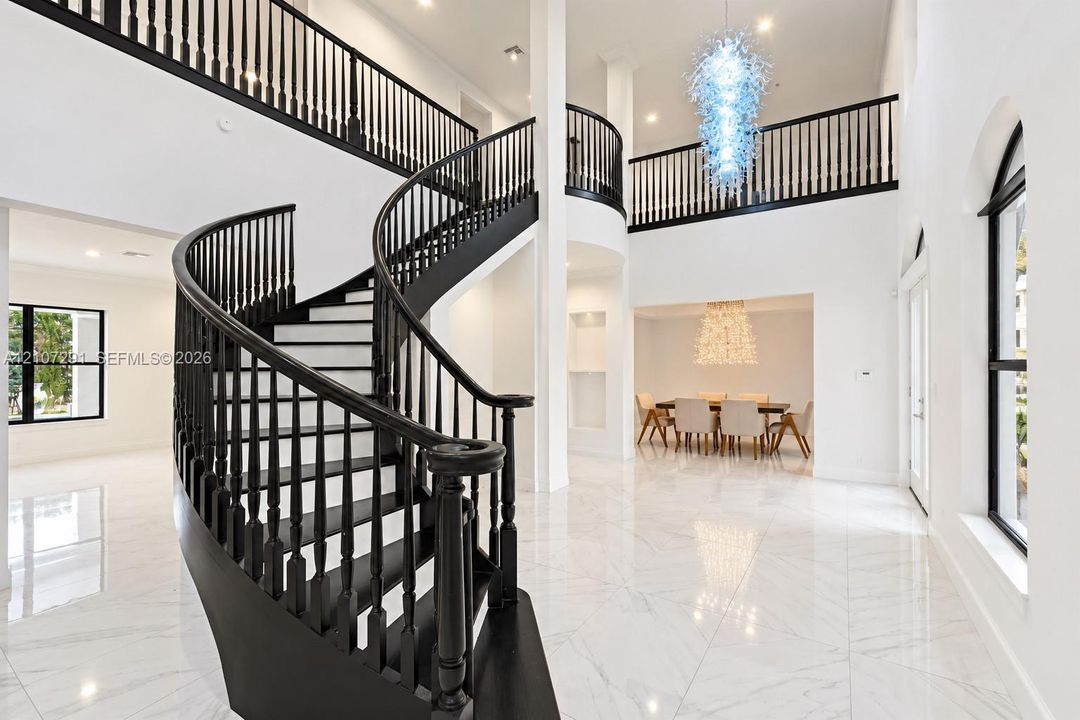 Foyer featuring a curved staircase with black railings, high ceilings, large-format tile flooring, recessed lighting, and a multi-tiered glass chandelier