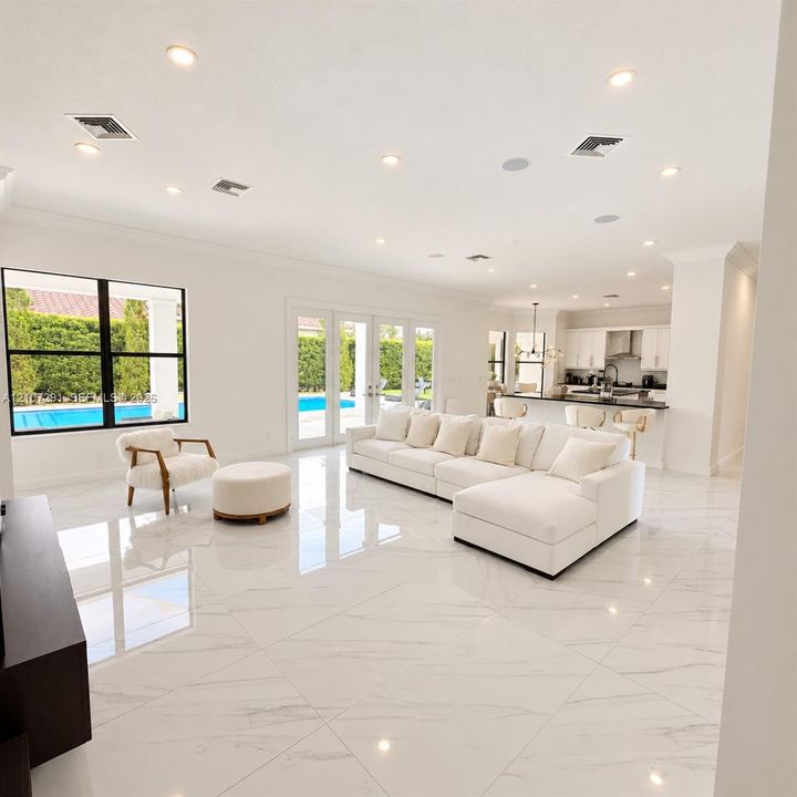 Open-concept interior featuring large-format stone-finish tile flooring, recessed ceiling lighting, kitchen breakfast bar with stone countertop, and multi-panel glass doors providing access to the pool area