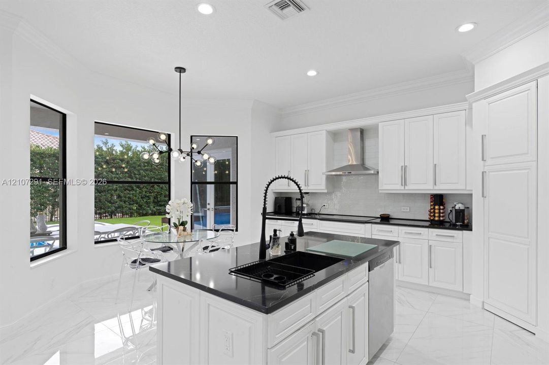 Kitchen featuring white shaker-style cabinetry, contrasting dark stone countertops, a center island with an integrated dark sink, large-format tile flooring, and a modern multi-light chandelier