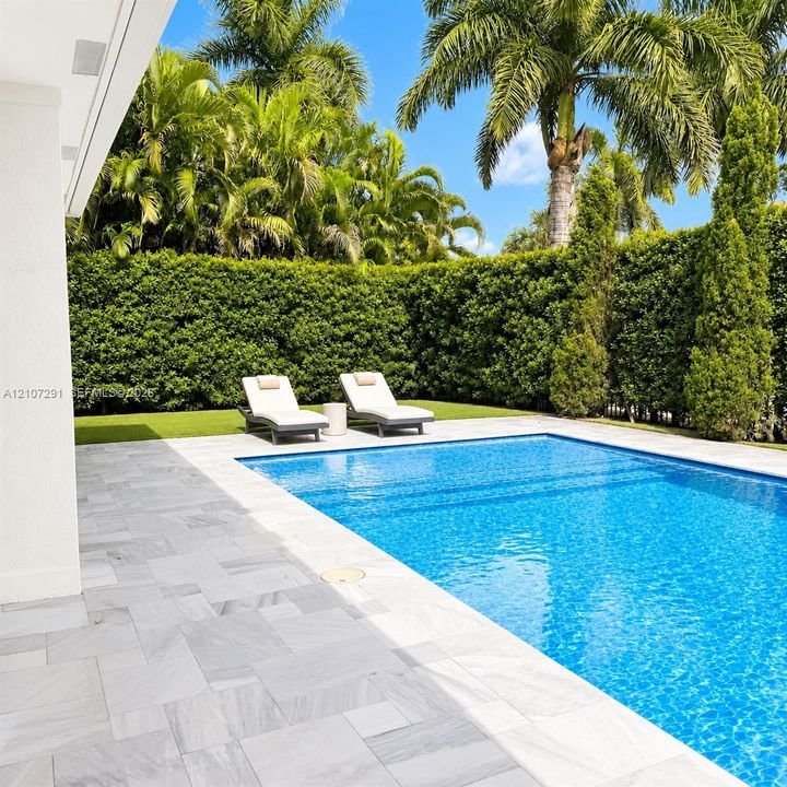 Rectangular swimming pool featuring large-format stone pavers, integrated lawn area, and perimeter privacy hedges