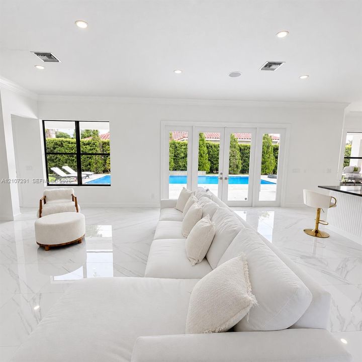 Polished stone-finish flooring, recessed lighting, expansive glass-paneled double doors, and black-trimmed windows