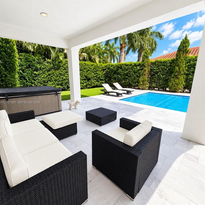 Covered patio with stone-finish tile flooring, inground swimming pool, integrated spa, and manicured privacy hedge